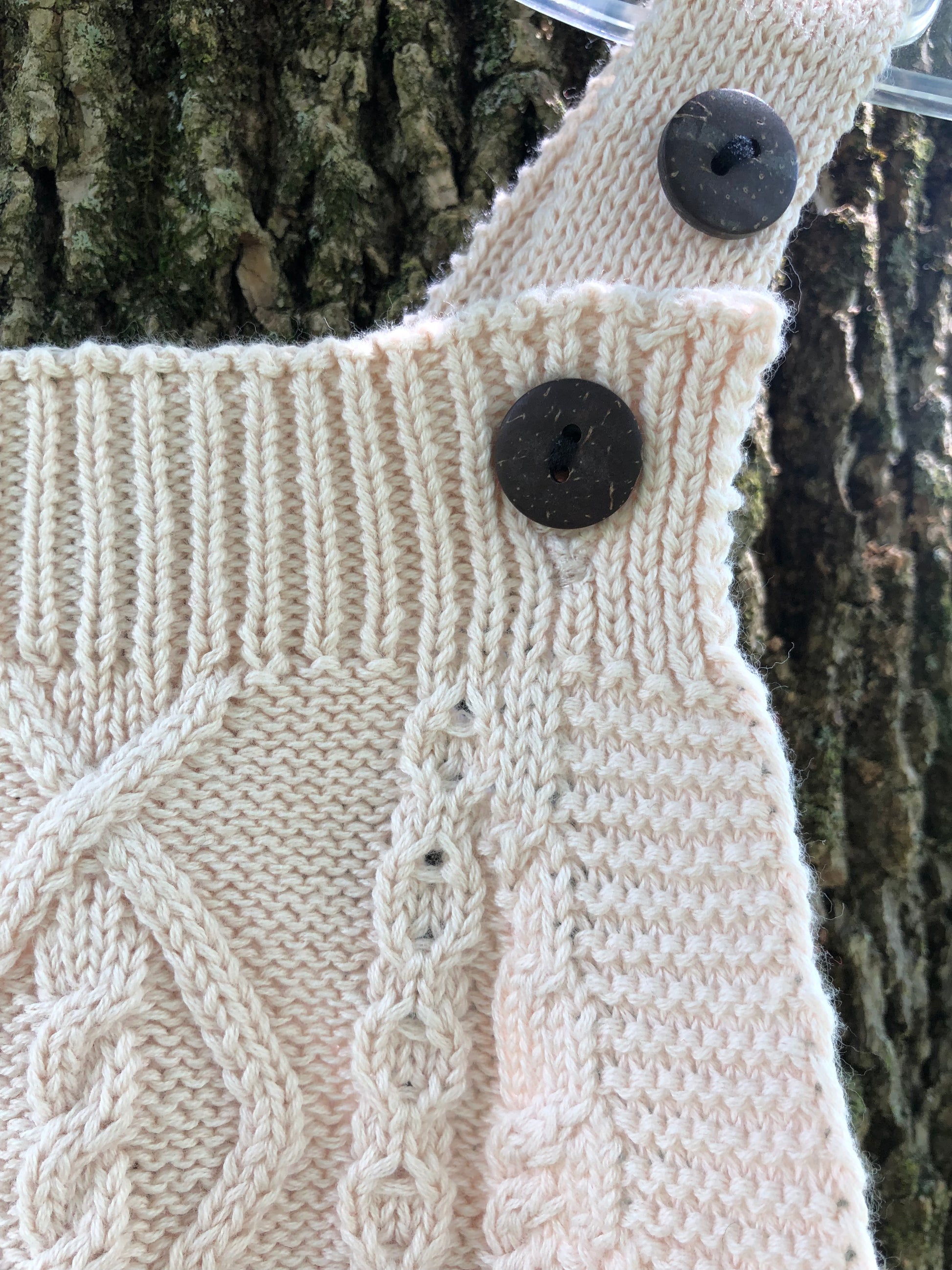 top of cream knit romper with adjustable wooden buttons hanging on tree
